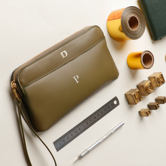 Green wristlet with initials on a light surface with stationery items