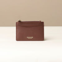 front view of a pebble leather card case nirua in brown with gold accents over a beige background