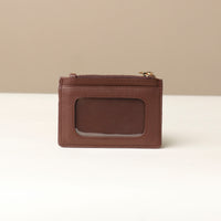 back view of a pebble leather card case nirua in brown with gold accents over a beige background