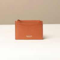 front view of a pebble leather card case nirua in light brown brown with gold accents over a beige background