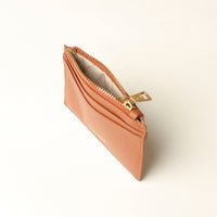 upper view of a open pebble leather card case nirua in light brown brown with gold accents over a beige background