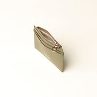 upper view of a open nappa leather card case nirua in olive green brown with gold accents over a beige background