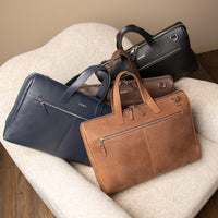 Three leather briefcases in black, brown, and tan colors placed on a white chair with a textured surface.