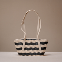 A woven straw tote bag with black and beige horizontal stripes and light beige shoulder straps, set against a neutral beige background.
