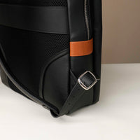 Black backpack with a brown strap and silver buckle on a light gray background