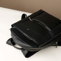 Black leather backpack on a white surface with a neutral background