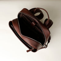 Brown leather backpack with open front pocket on a light beige background