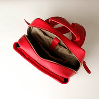 Red leather handbag with open front pocket on a light beige background
