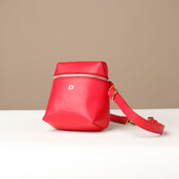 Red leather bag with a gold zipper and strap on a beige background