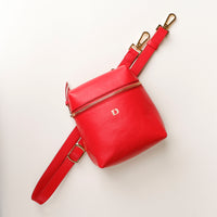 Red leather bag with gold zipper and strap on a light beige background