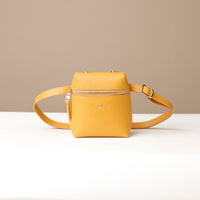 Yellow crossbody bag on a white surface with a beige background