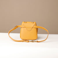 Yellow handbag with a strap on a white surface and beige background