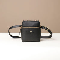 Black leather crossbody bag with gold zipper and buckle on a beige background