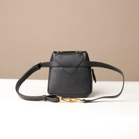Black leather handbag with gold clasp on a beige background