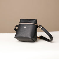 Black leather bag with gold zipper and strap on a beige background