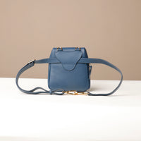 Blue leather handbag with a strap on a white surface and beige background