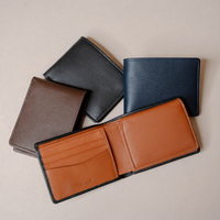 Four leather bifold wallets arranged on a light beige background, with one wallet open in front to show the interior. The wallets are in black, navy blue, brown, and tan/cognac, all with a pebbled texture and black edges.