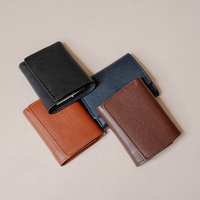 Four pebbled leather bifold wallets in black, navy blue, tan, and brown, arranged in a flat-lay pattern on a light beige background.