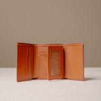 An open tan leather bi-fold wallet with multiple card slots, a side pocket, and a clear ID window showing a quilted interior lining, set against a neutral beige background.