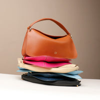 A stack of three handbags in different colors, with the top bag being brown and the bottom ones in black and blue. Each bag has a sleek design with a fold-over closure.