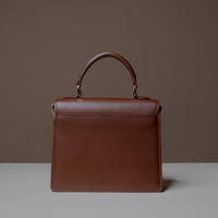 Back View of Brown Nelda Bag elegant leather handbag with detachable shoulder strap on a gray surface with a brown background