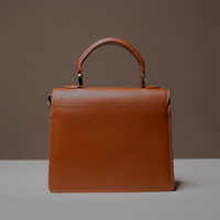 Back View of Brown Nelda Bag elegant leather handbag with detachable shoulder strap on a gray surface with a brown background