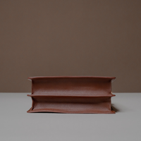Bottom View of Brown Nelda Bag elegant leather handbag with detachable shoulder strap on a gray surface with a brown background