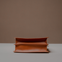 Bottom View of Brown Nelda Bag elegant leather handbag with detachable shoulder strap on a gray surface with a brown background