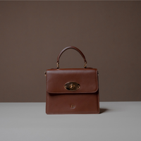 Front View of Brown Nelda Bag elegant leather handbag with detachable shoulder strap on a gray surface and brown background