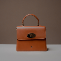 Front View of Brown Nelda Bag elegant leather handbag with detachable shoulder strap with a gold clasp on a gray surface and brown background