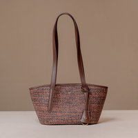 A structured woven handbag with a brown and beige tweed body, dark brown leather handles, and a small gold-tone logo charm, set against a solid beige background.