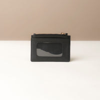 back view of a pebble leather card case nirua in black with gold accents over a beige background