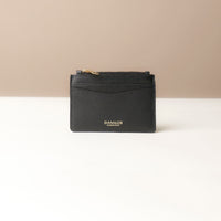 front view of a pebble leather card case nirua in black with gold accents over a beige background