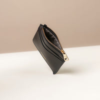 upper view of a open pebble leather card case nirua in black with gold accents over a beige background