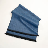 Folded blue fabric with black fringe on a white background