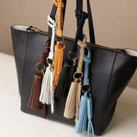 A collection of leather tassel charms in various colors attached to a black handbag.