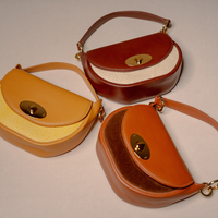 Three vintage-style semi-circular shoulder bags in warm leather tones, arranged on a light beige background. One bag is mustard yellow with a cream chevron panel; one is dark reddish-brown with a cream panel; the third is tan/caramel brown with a dark brown suede-like front panel.