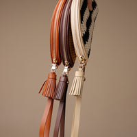 Four zipped pouches with tassels in brown, beige, and black and white pattern on a beige background.