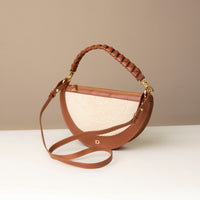 Brown handbag with braided handle and detachable strap on a neutral background.