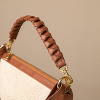 Close-up of a brown handbag handle with gold hardware on a beige background.