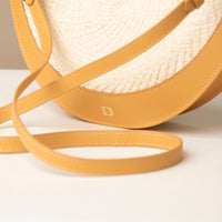 Close-up of a straw bag with yellow straps on a light background.