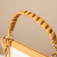 Close-up of a braided handbag handle on a beige background.