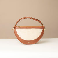 A crescent-shaped shoulder bag with a short handle featuring hand-woven details and a long, adjustable strap. The bag is made with natural fibers and has a zipper closure.