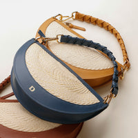 Blue handbag with straw-like interior and tan braided handle on a light background