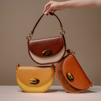 Three crescent-shaped shoulder bags in brown, tan, and orange-brown leather with woven beige panels and gold-tone turn-lock closures, displayed on a beige studio background. A hand is holding the top brown bag.