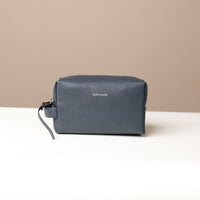 A blue leather toiletry bag with a zipper closure and a small leather strap, displayed against a neutral background.