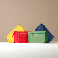 Four colorful handbags (yellow, red, green, blue) on a white surface with a beige background.