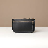 Black leather pouch with gold zipper on a beige background