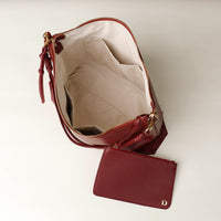 Maroon handbag with open zipper on a light beige background