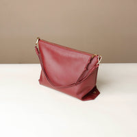 Maroon handbag on a white surface with a beige background